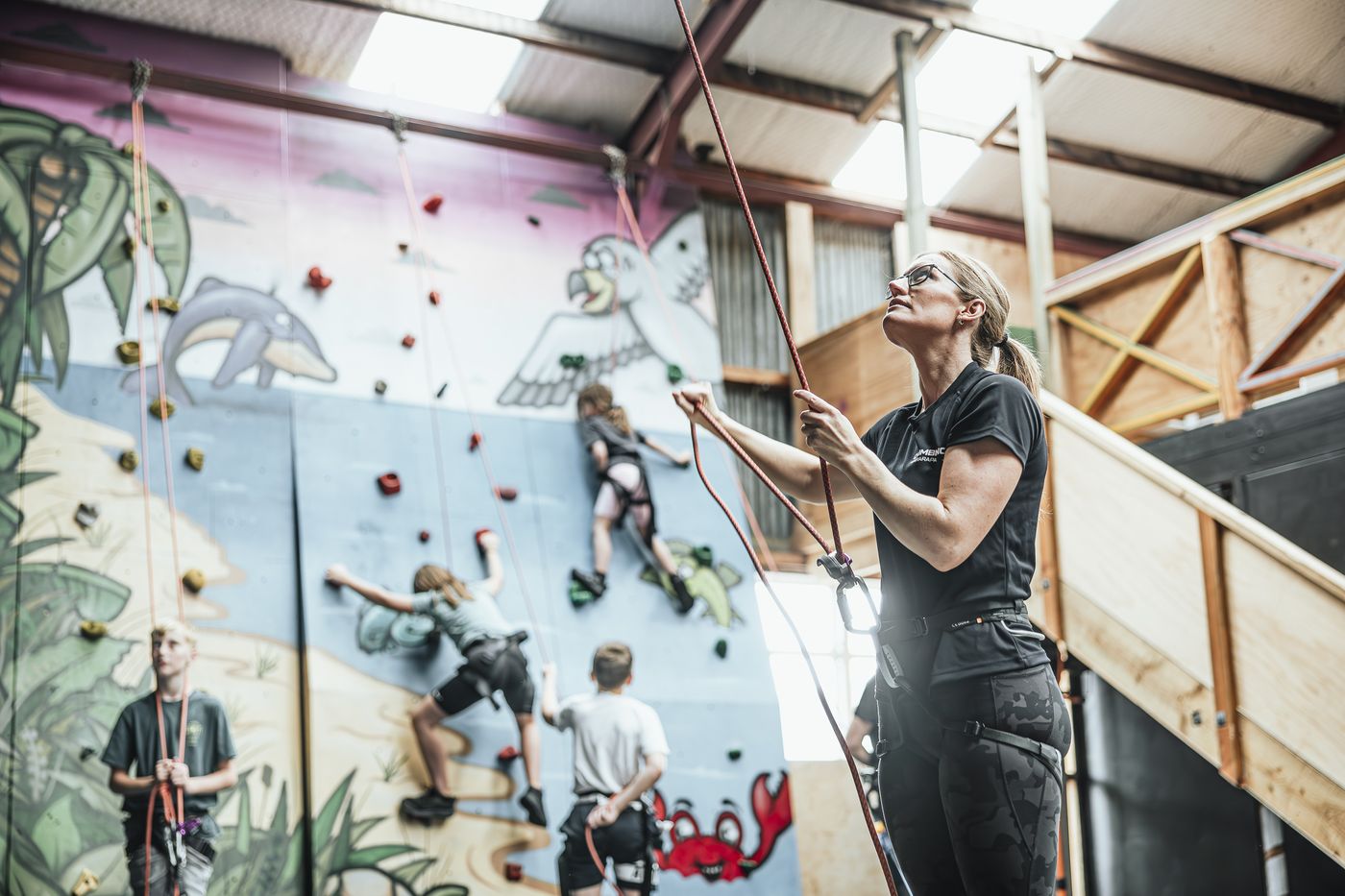 An instructor belaying while a group climbs the mural wall