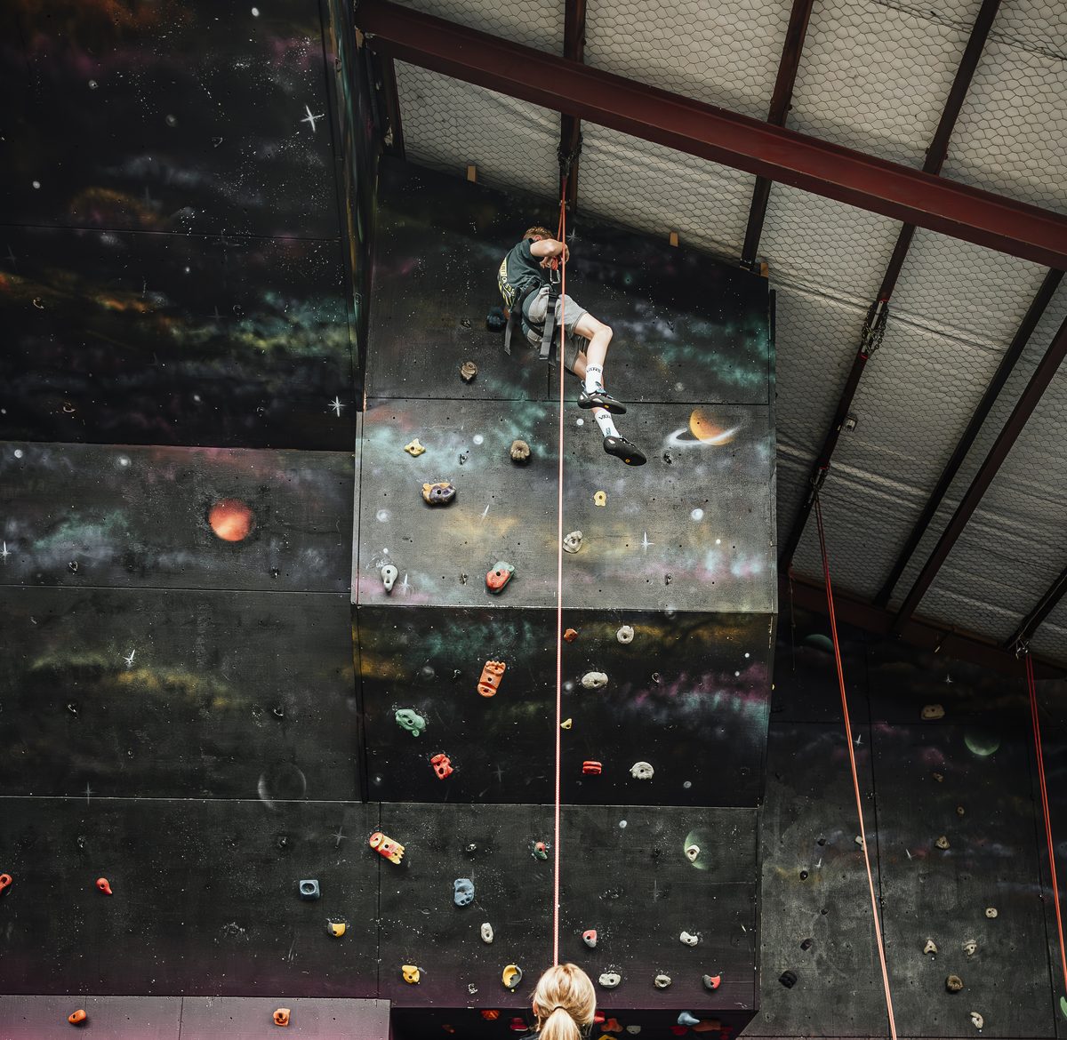 An instructor belaying while a young climber abseils down the mural wall